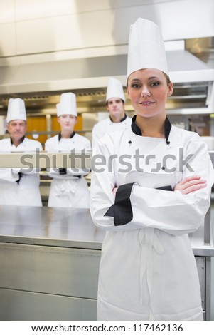 Smiling chef with crossed arms with team standing behnd her