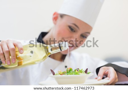 Smiling woman chef dressing a salad in the kitchen