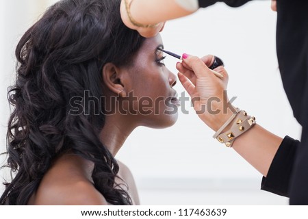 Woman sitting while getting her eyebrows done by makeup artist