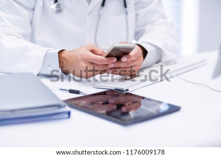 Mid section of doctor using mobile phone in clinic