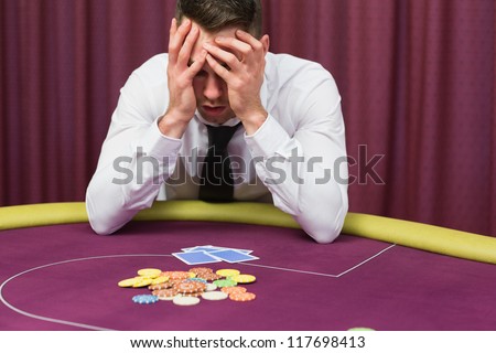 Man holding head in hands at poker table in casino