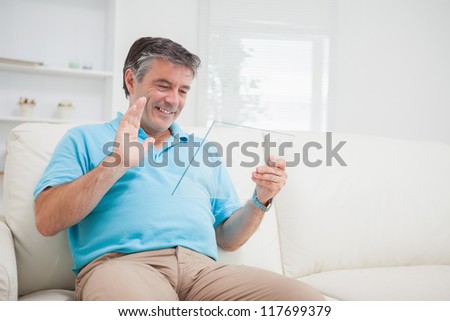 Smiling man using video chat waving at clear pane as digital tablet pc