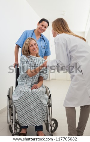 Smiling female patient shaking hand of doctor with nurse in hospital corridor
