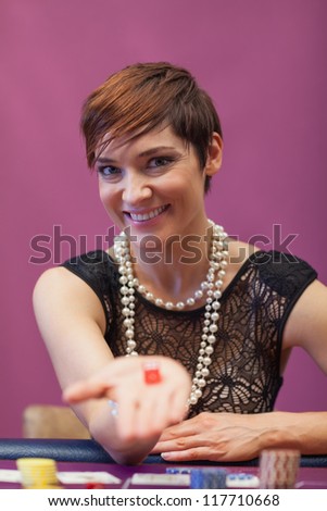 Woman sitting in a casino at table while holding dices and smiling