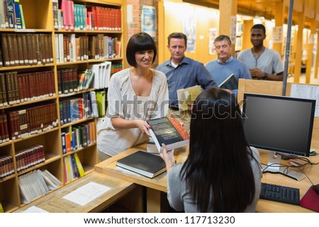 Librarian handing book to woman at library desk