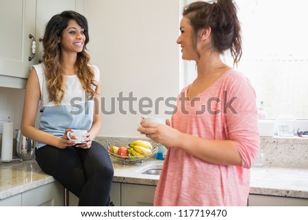 Friends chatting in kitchen over coffee standing and sitting on counter in kitchen
