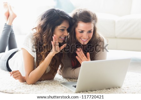 Two women using video chat on laptop waving at screen on floor