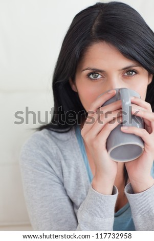 Close-up of a woman drinking from a mug that she holds with two hands in a living room