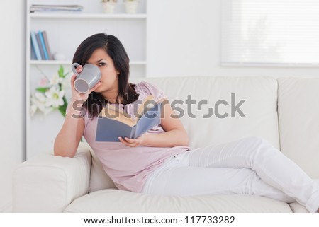 Woman drinking from a mug while lying on a sofa in a living room