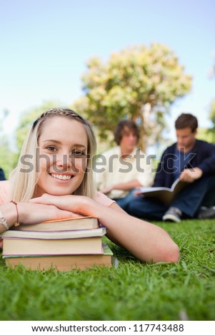 Close-up of a girl lying head on her books in a park with friends in background