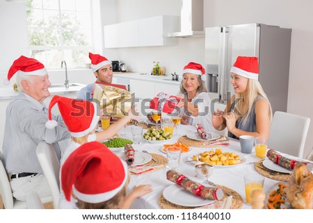 Family wearing santa hats swapping christmas presents at dinner table
