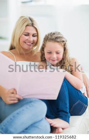 Mother sitting on the sofa with her daughter while reading book