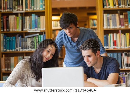 Students watching something on laptop in library in college