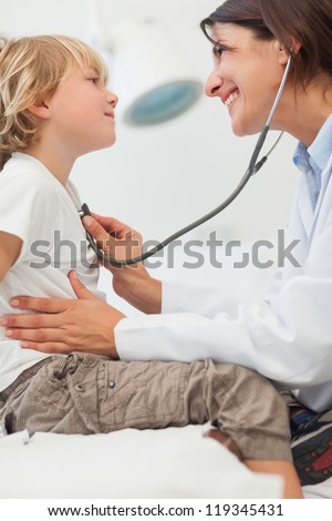 Smiling Doctor Auscultating A Child With A Stethoscope In Examination Room