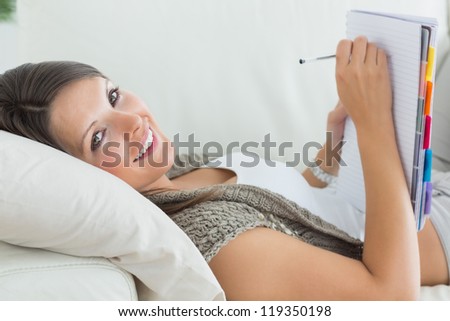Happy woman lying on sofa and writing in the living room