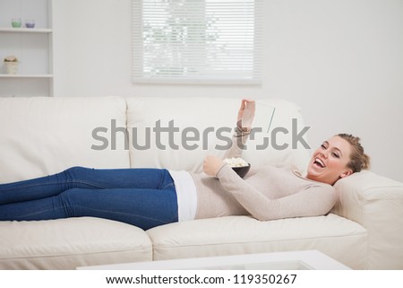 Smiling woman laughing at the clear pane as tablet pc while lying on the sofa