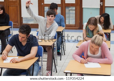 Student raising hand during exam in exam hall in college