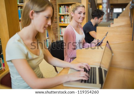 Woman using tablet pc looking up from studying in college library