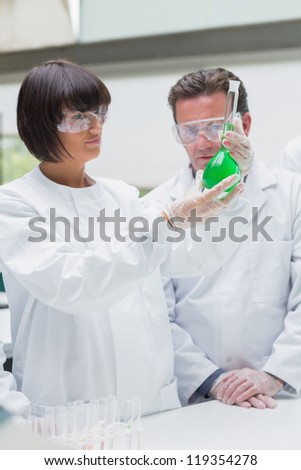 Chemists viewing  green liquid in beaker in the lab