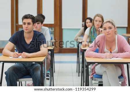 Students sitting at desk looking up in exam hall in college