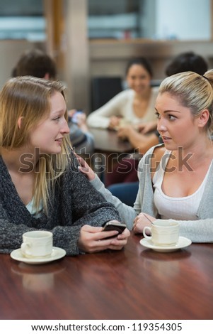 Student comforting upset friend with mobile phone in college cafe