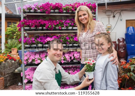 Employee presenting flower pot to little girl with mother in the garden center