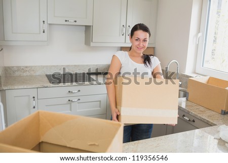 Young woman unpacking in kitchen holding box