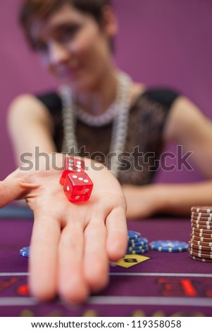 Woman sitting in a casino at table holding dices while smiling