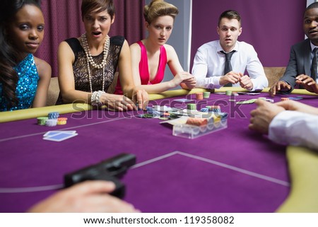 People looking scared at gun on poker table in casino