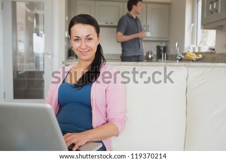 Young woman using the laptop on the couch while the man stands in the kitchen