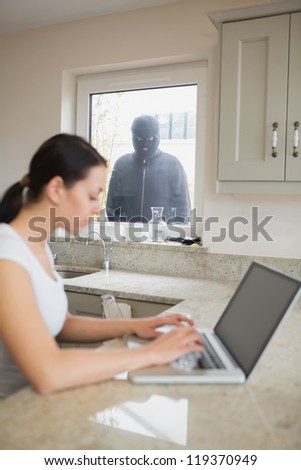 Young woman using her laptop and is observed by a robber at the window