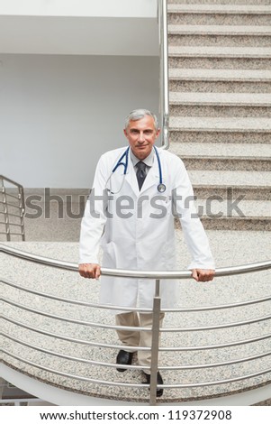 Smiling doctor  leaning on the railing of the stairs in the hospital
