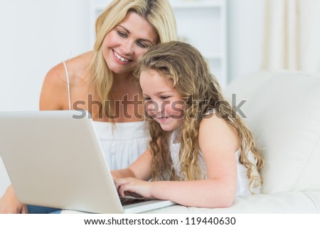 Smiling daughter and mother working with notebook