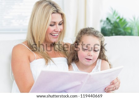 Smiling daughter and mother reading book on the sofa