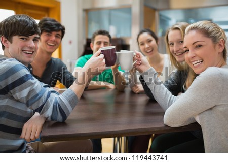 Students sitting clinking cups while smiling in college cafe