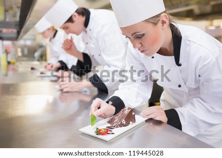 Chef\'S Team Garnishing Slices Of Cake In The Kitchen