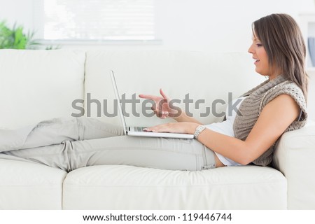 Woman using video chat on laptop lying on the sofa