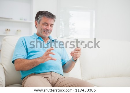 Smiling man relaxing on the couch while holding a clear pane as a tablet pc