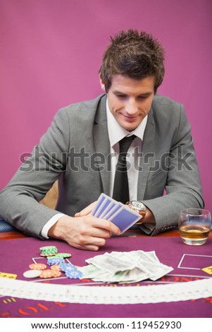 Smiling man sitting at table in a casino while playing poker and holding cards