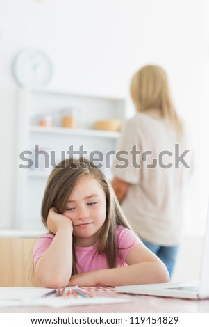 Little girl bored with drawing with mother in background