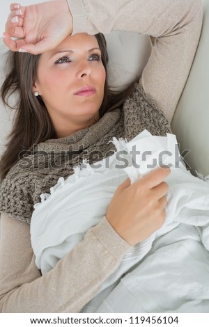 Ill woman lying on sofa with blanket holding a tissue feeling sorry for herself