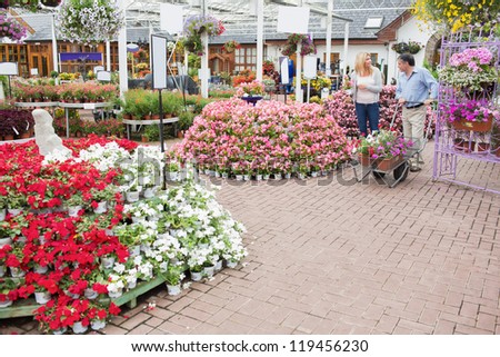 Outside of garden center with many types of plants and flowers and couple pushing a trolley