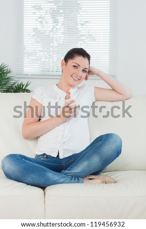 Smiling woman sitting on the couch cross legged and holding a cup of coffee