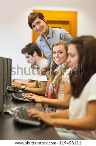 Students sitting at the computer while teacher smiling in college