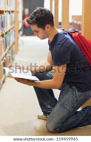 Student kneeling by bookshelf in library looking at a book in the library
