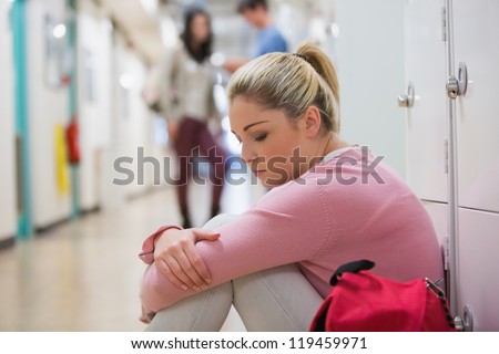 Student sitting on the floor at the hallway looking disappointed eyes closed