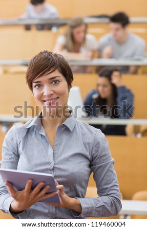 Woman standing holding a tablet computer smiling at the lecture hall