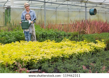 Gardener and gradnchild holding a watering can in greenhouse