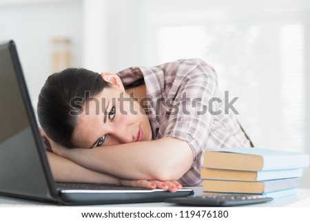 Tired woman leaning on laptop in living room