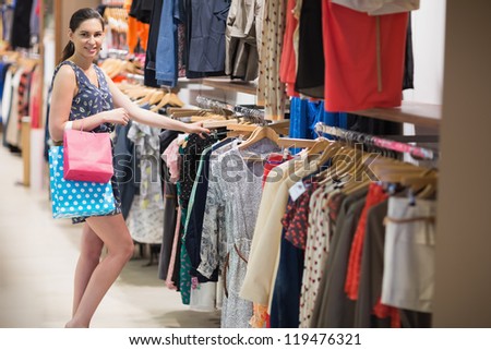 Woman searching through clothes rail at the boutique while holding two bags